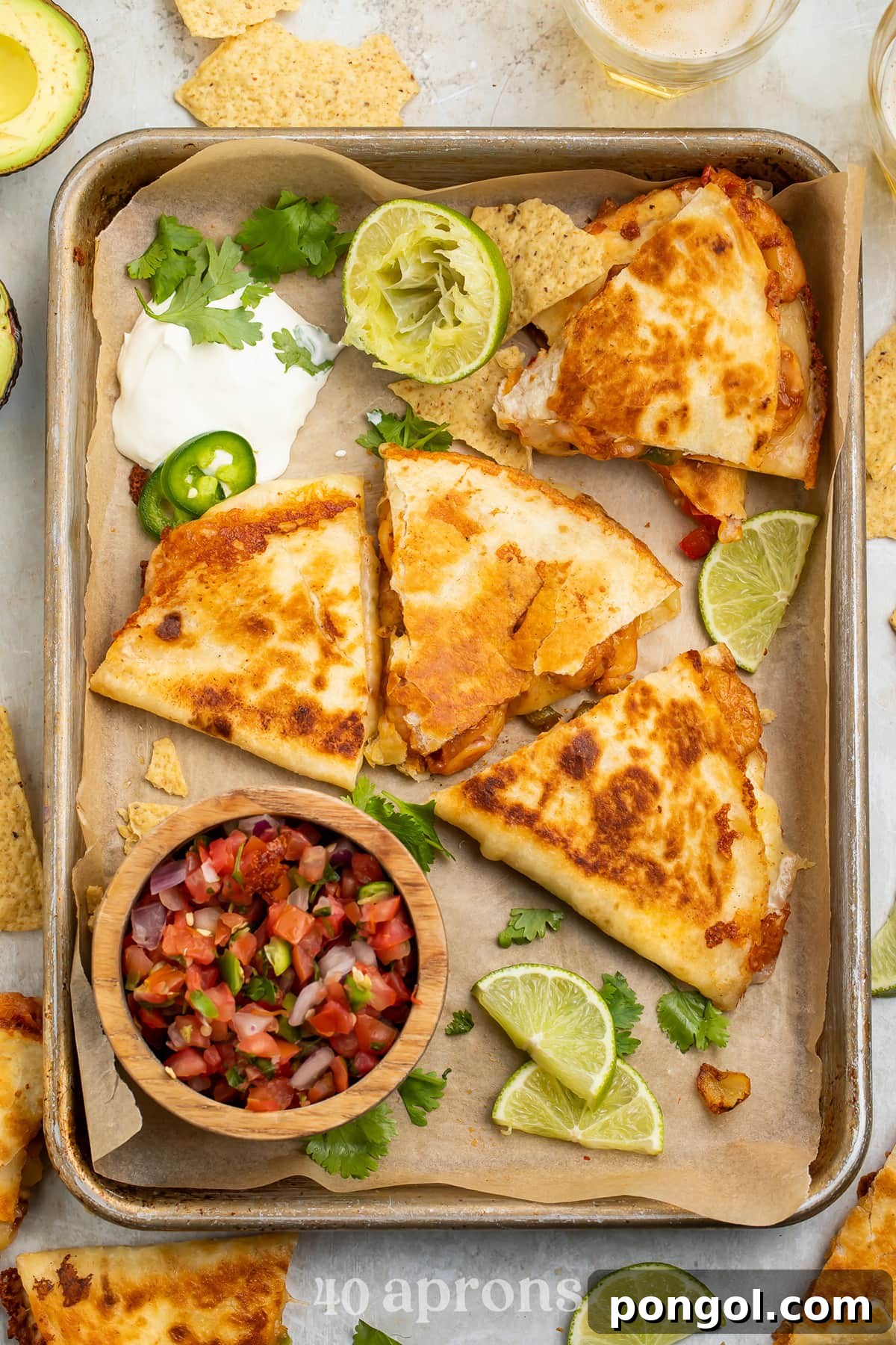 Overhead view of a shrimp quesadilla cut into 3 wedge-shaped slices surrounded by toppings like cilantro, lime, and pico de gallo.