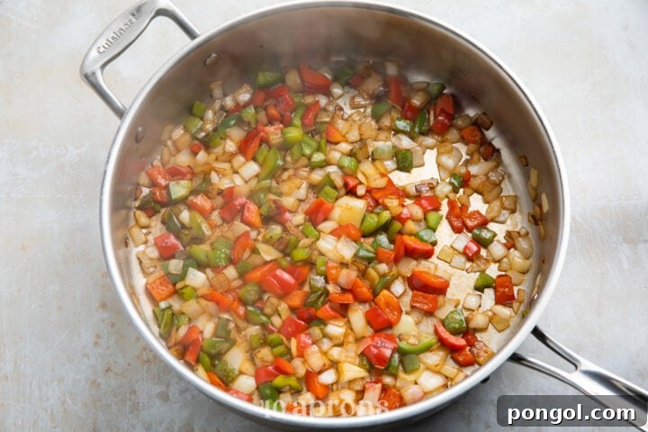Onion and pepper mixture sautéing in a large silver skillet for shrimp quesadillas.