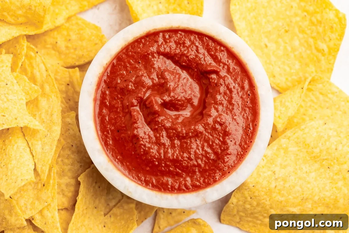 Rich, vibrantly red smoky guajillo salsa in a small bowl surrounded by golden tortilla chips, ready for dipping.