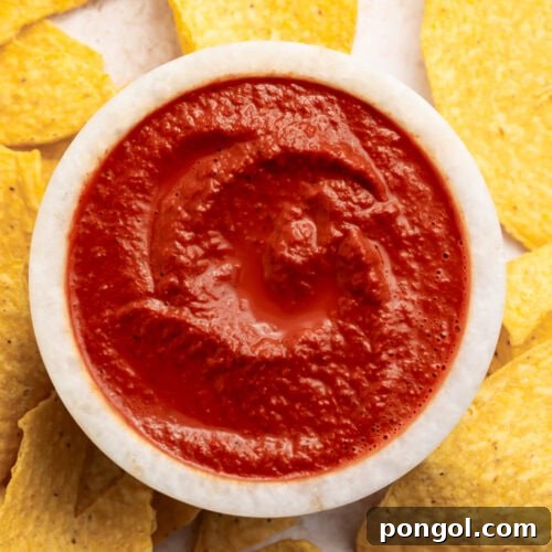 Rich, vibrantly red smoky guajillo salsa in a small bowl surrounded by tortilla chips.