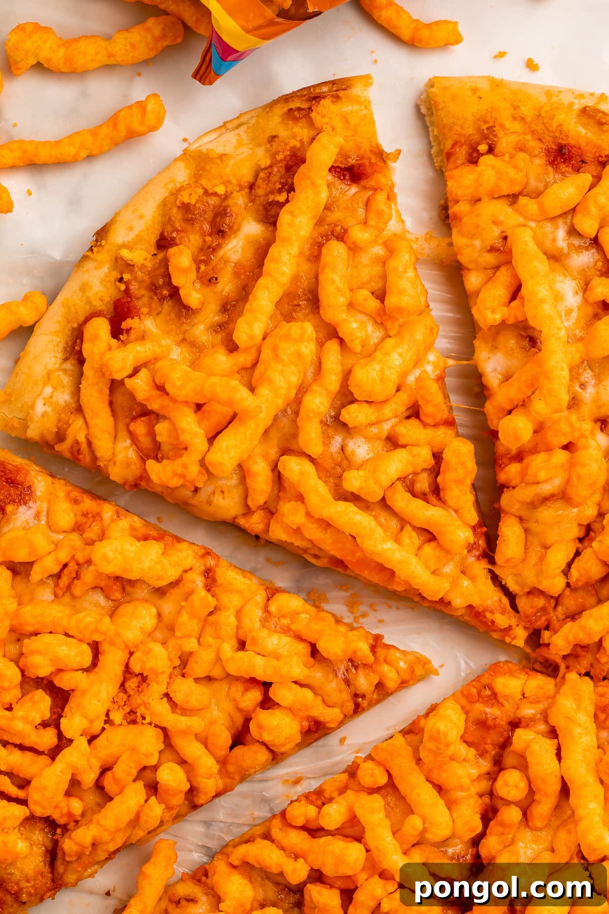 A vibrant slice of Cheeto pizza being lifted from the whole pie, showcasing the crunchy orange topping and melted cheese.