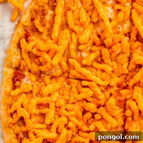 A large round cheese pizza topped with bright orange crunchy Cheetos, cut into triangle-shaped slices but still together as a whole pizza.