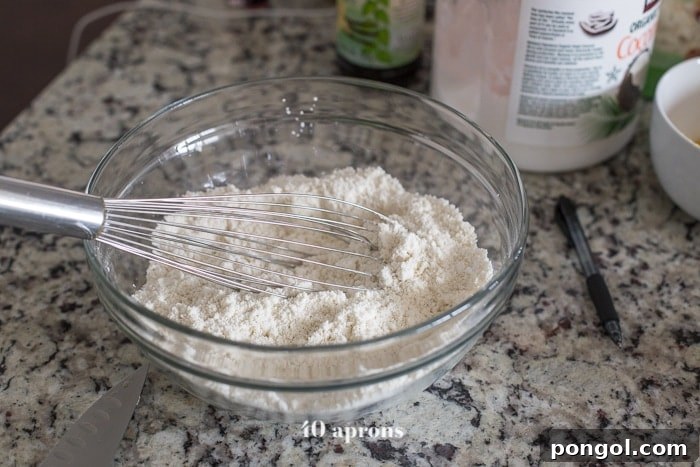 Dry ingredients for paleo waffles, including almond, tapioca, and coconut flours, baking powder, and salt, whisked in a bowl.