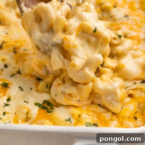 A spoonful of green chili mac and cheese being lifted out of a casserole dish, highlighting its creamy texture.