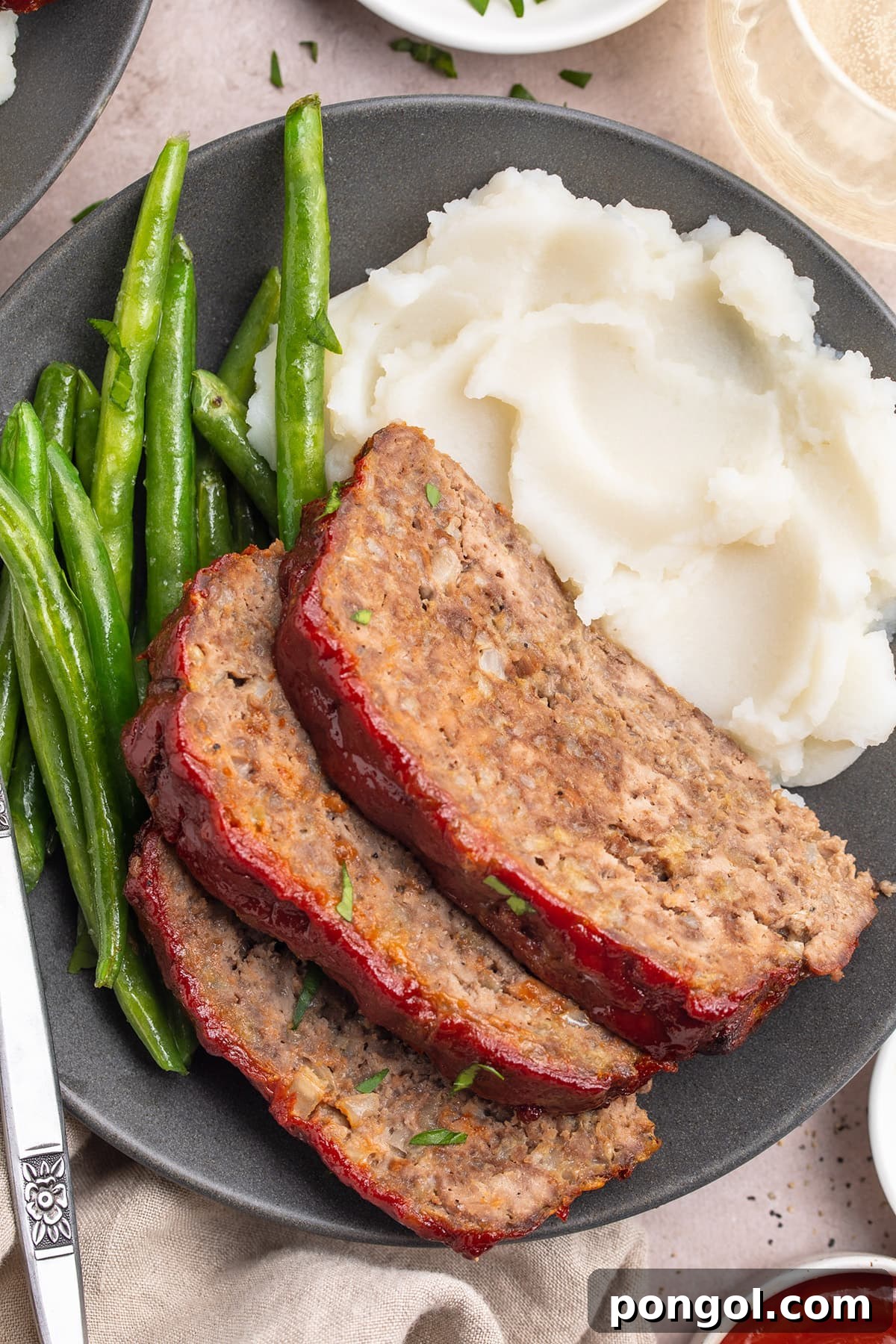 Hearty Gluten-Free Meatloaf 2 Three slices of gluten-free meatloaf topped with ketchup and plated with mashed potatoes and fresh green beans.