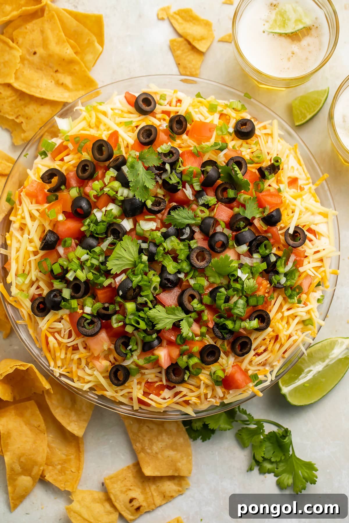 Top-down view of a large glass bowl of 7 layer dip topped with olives and green onions.