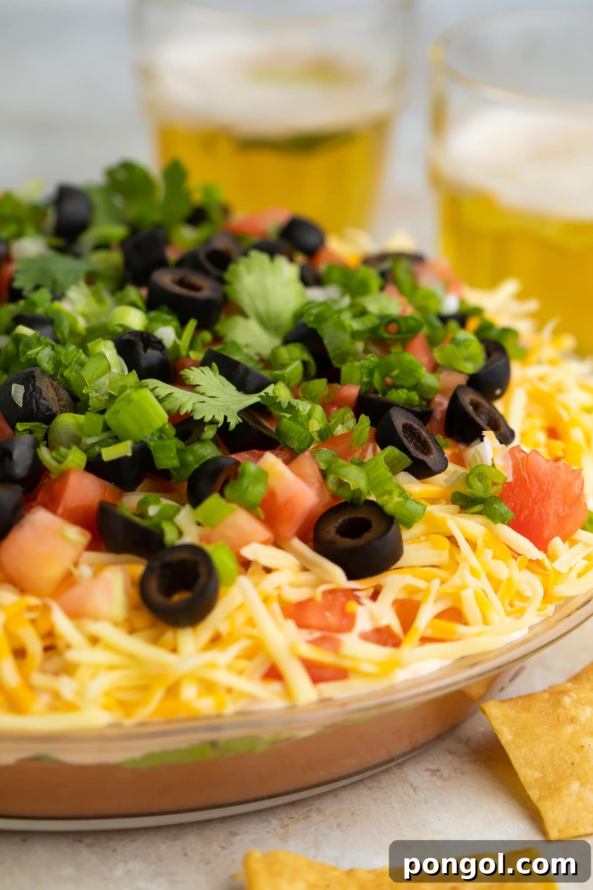 A side-view of a large glass bowl filled with a 7 layer dip.