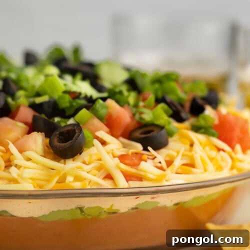 A side-view of a large glass bowl filled with a 7 layer dip.