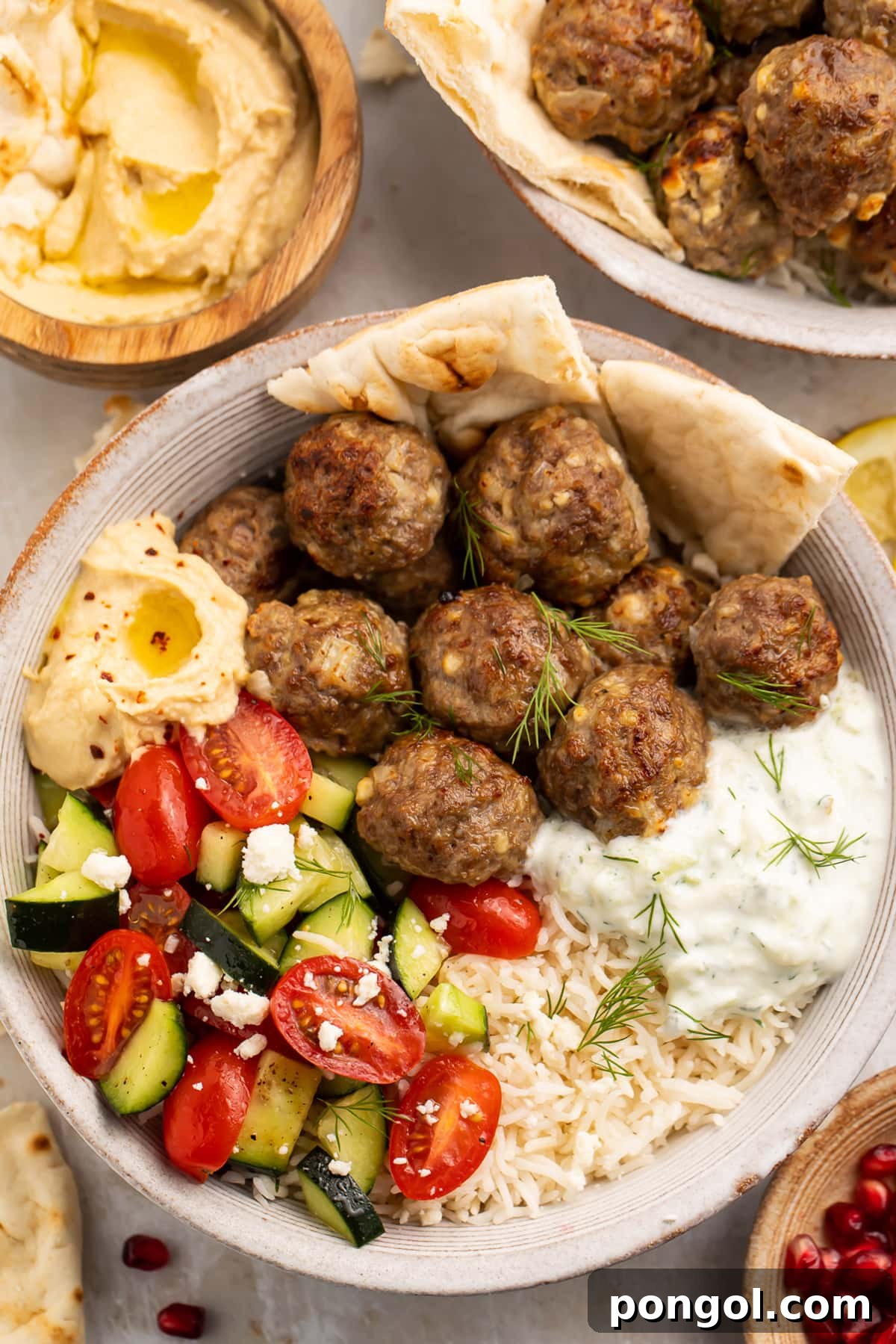 Gyro meatballs in a bowl with tomato and cucumber salsa, tzatziki, naan, and hummus.