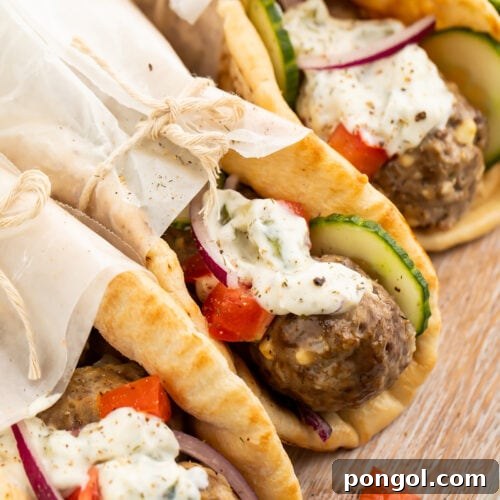 Three pitas stuffed with gyro meatballs, tzatziki, cucumber, and tomatoes, wrapped in parchment paper.