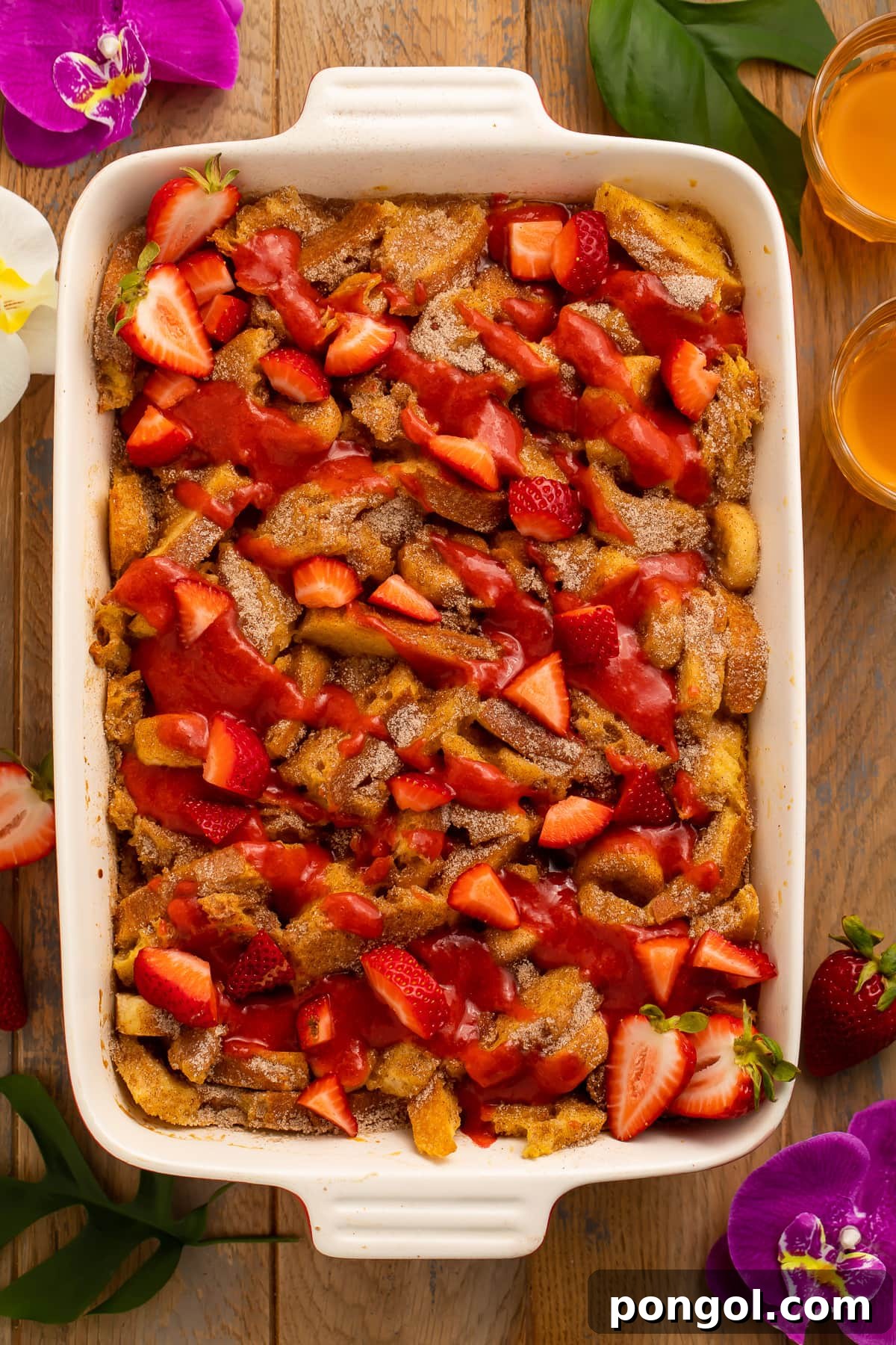 An inviting overhead view of a large casserole dish brimming with golden French toast, sliced bananas, and fresh strawberries, ready to be served.