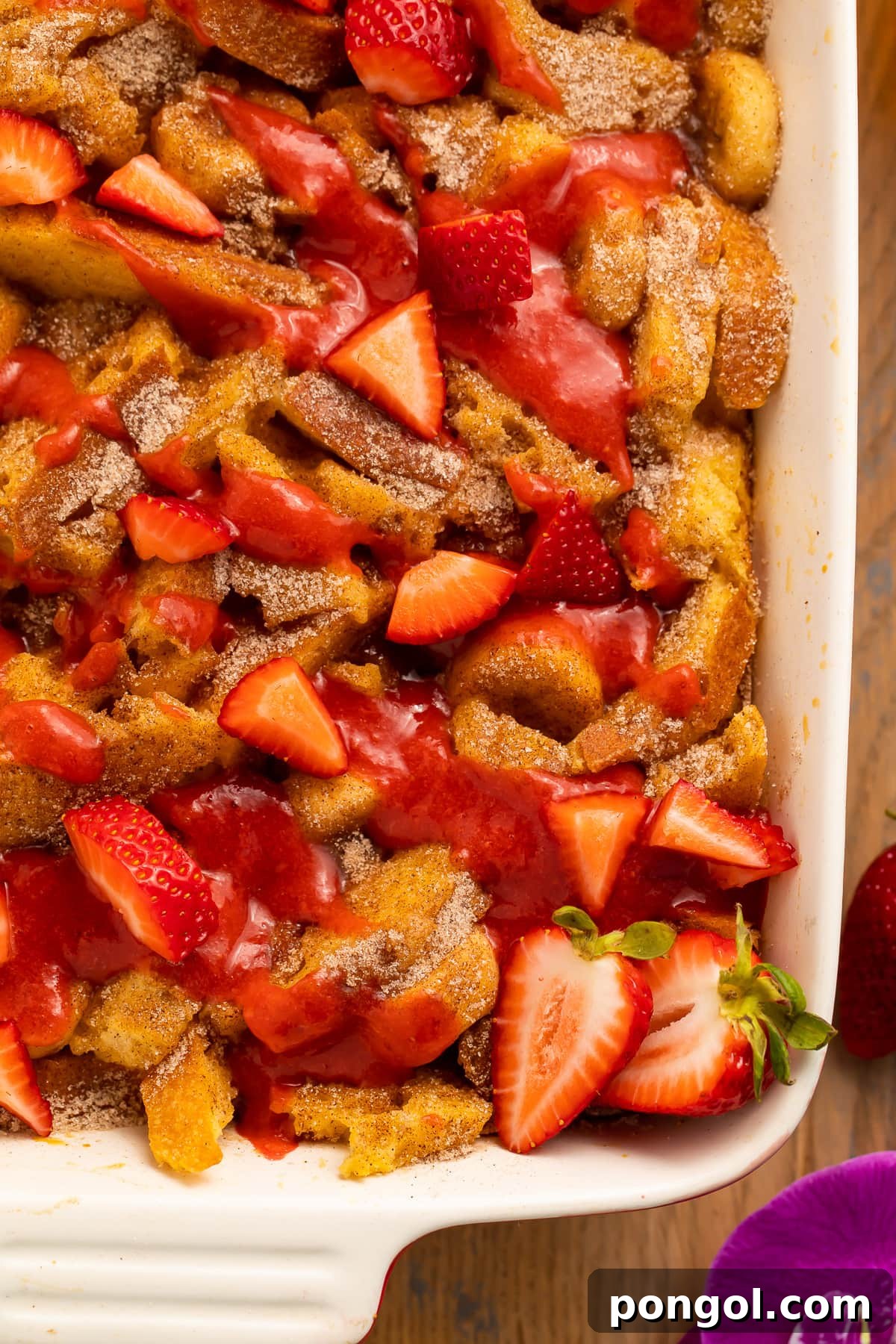 A beautifully set table featuring a golden-baked banana stuffed French toast casserole, generously topped with fresh strawberries and strawberry sauce.