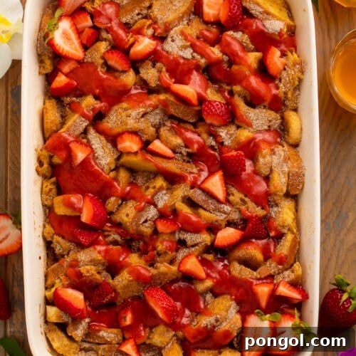 Overhead view of a large casserole dish filled with golden French toast, bananas, and strawberries.