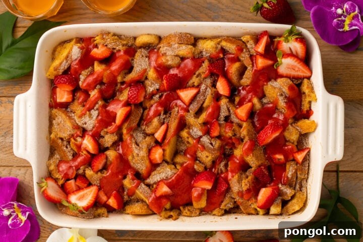 A close-up shot of the fully prepared Tonga Toast Casserole, garnished with strawberry sauce and fresh strawberries, ready for serving.