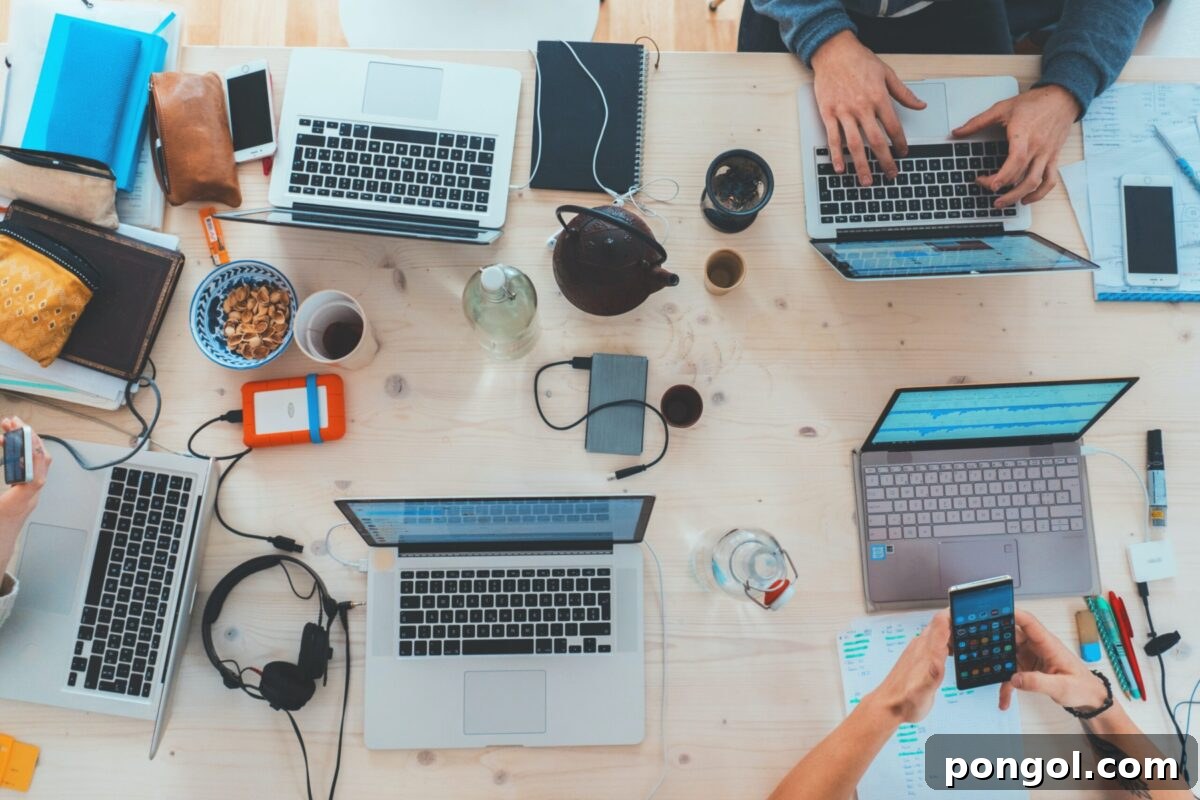 Laptops, phones, and tablets on a table with cups of coffee and people working.