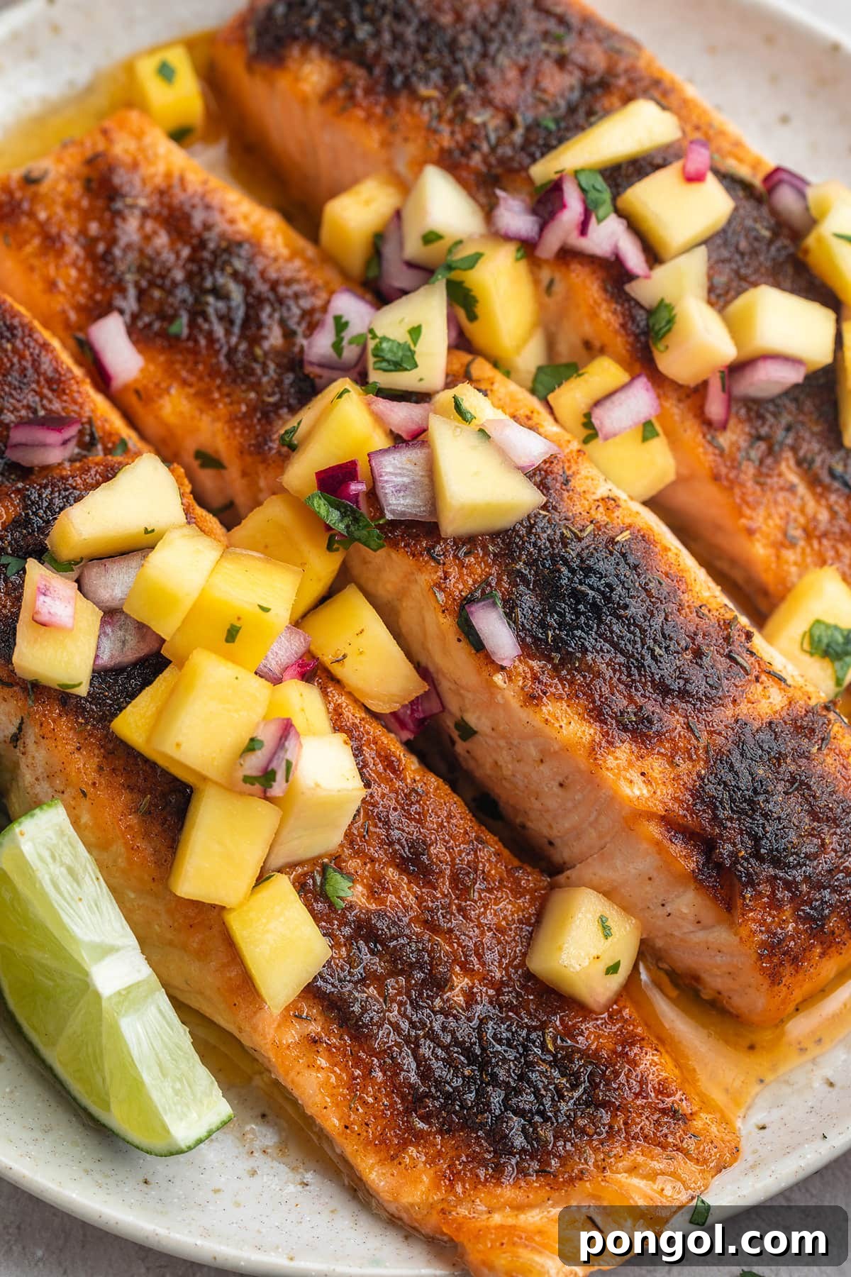 Three jerk salmon fillets topped with mango salsa on a round white plate.