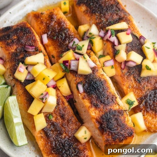 Three jerk salmon fillets topped with mango salsa on a round white plate.