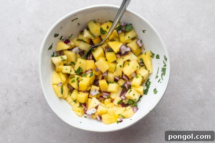 Mango salsa in a white bowl with a silver spoon.