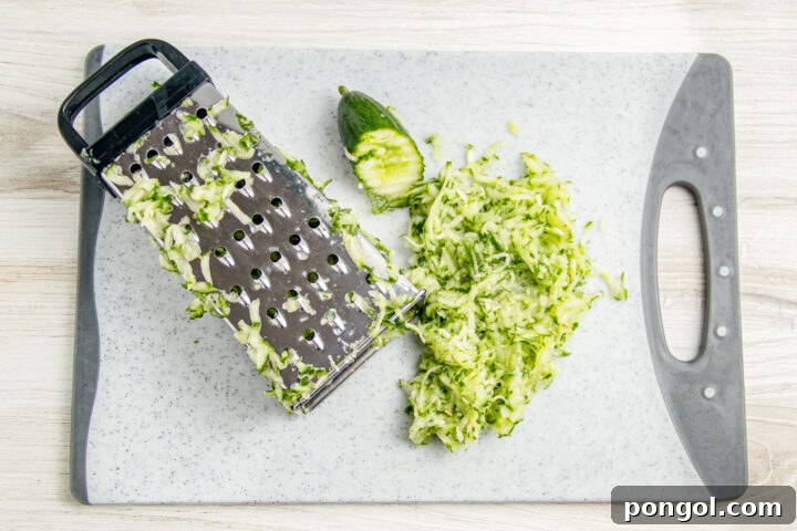Green, unpeeled cucumber grated onto a cutting board with a box grater.