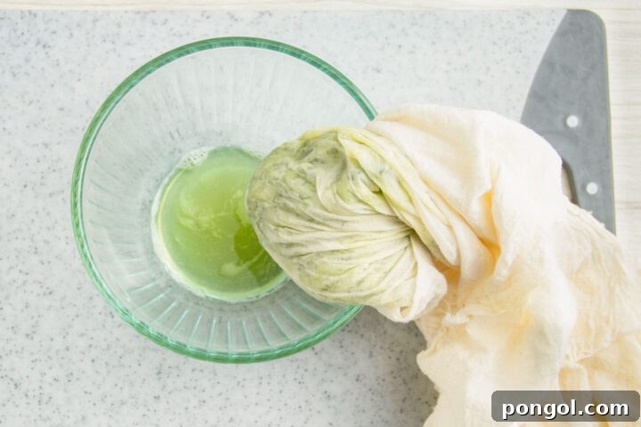 Pale green liquid in a small glass bowl next to grated cucumber in a cheesecloth.