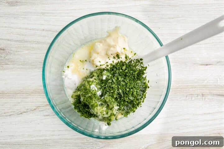 Ingredients for Whole30 tzatziki in a large glass mixing bowl with a white silicone spatula.