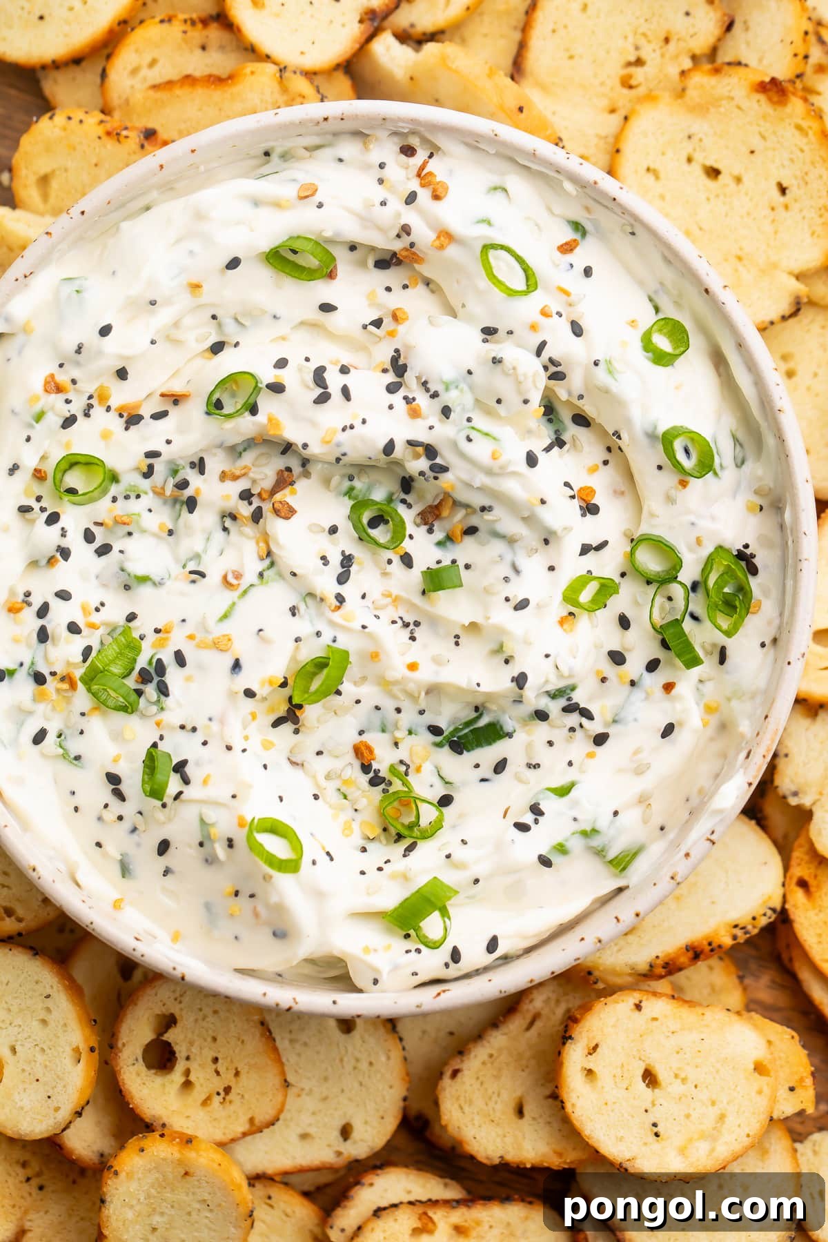 Overhead view of a bowl of Everything Bagel dip topped with Everything Bagel seasoning and green onions.