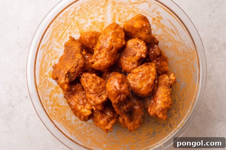 Golden Chicken Bites 10 Breaded, fried boneless chicken wings with buffalo sauce in a large glass mixing bowl.