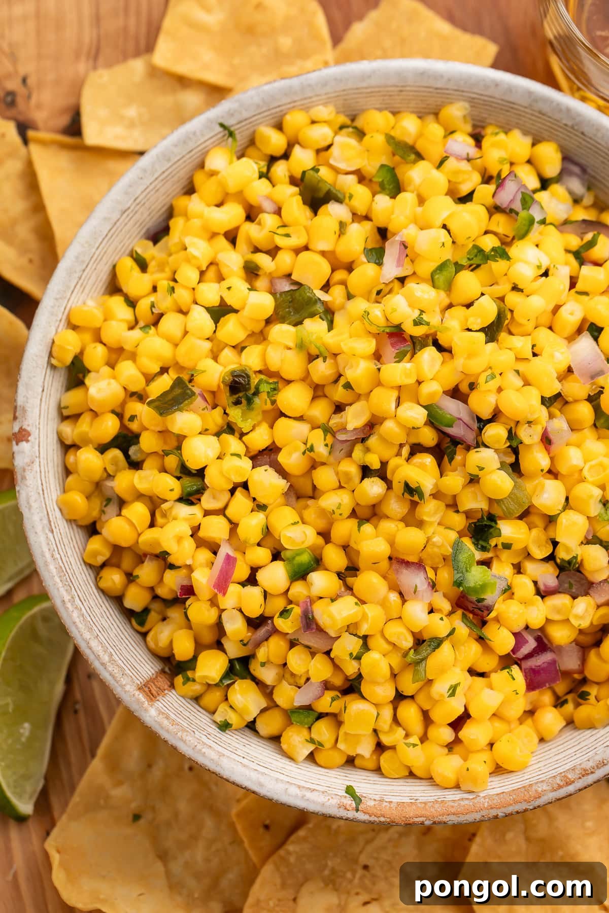 A bowl of vibrant homemade roasted chili corn salsa, perfectly garnished and ready to be served with a scattering of crunchy tortilla chips around it.