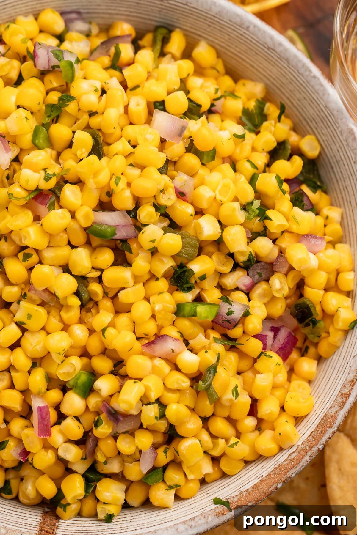 A close-up shot of the roasted chili corn salsa in a bowl, showing the vibrant colors and fresh ingredients, with more tortilla chips in the background.