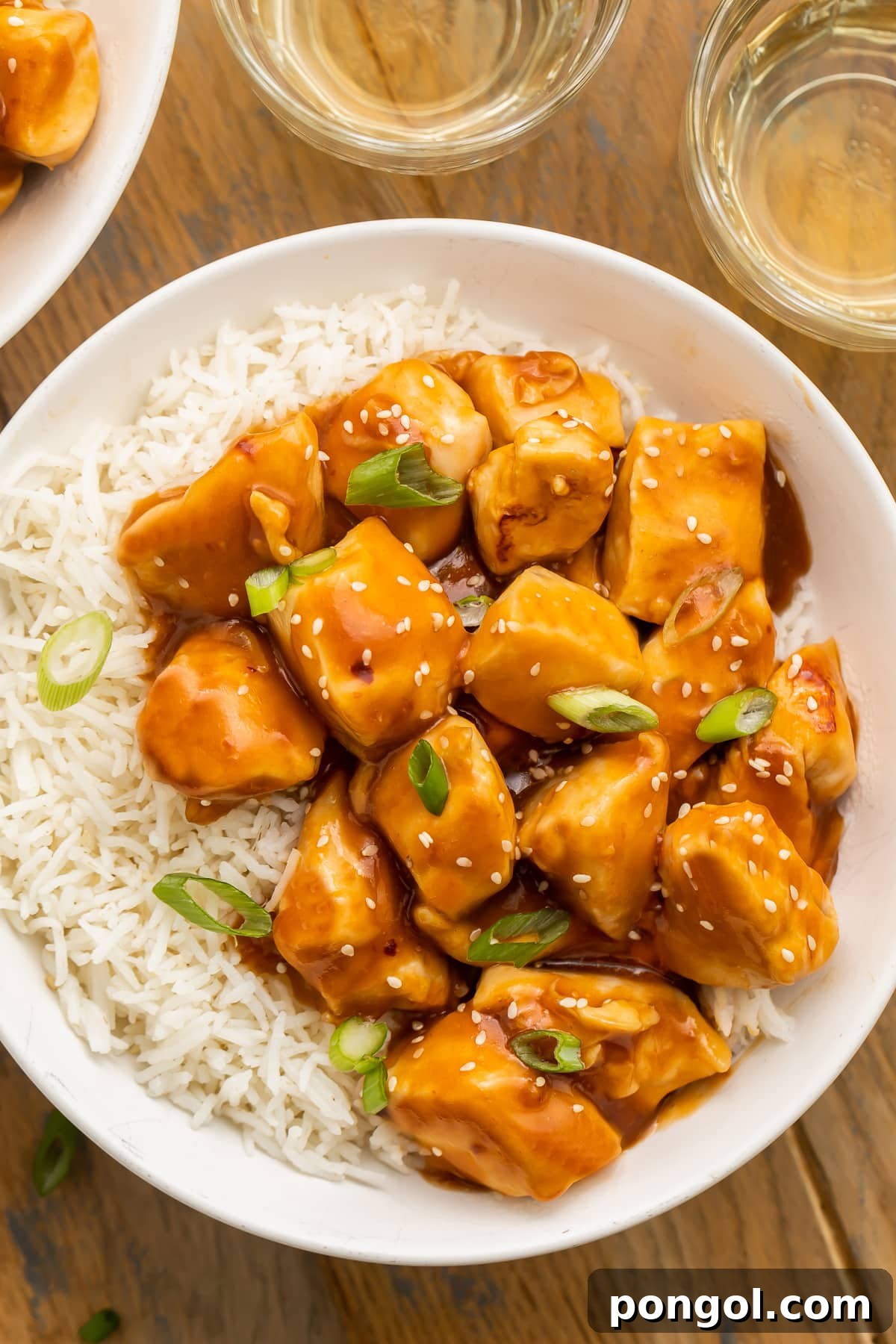 Vibrant orange glazed Instant Pot honey garlic chicken, garnished with fresh sesame seeds and thinly sliced green onions, served in a clean white bowl alongside fluffy white rice. The dish looks inviting and perfectly cooked, highlighting its rich, glossy sauce.