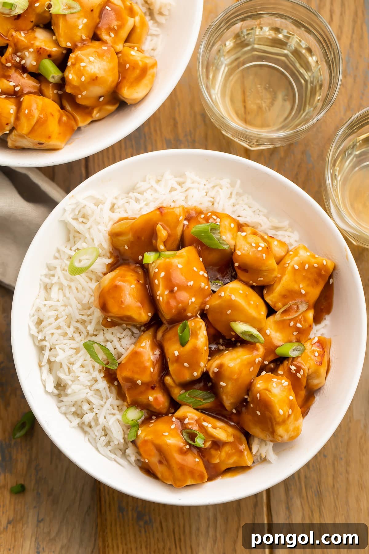 Close-up shot of the Instant Pot Honey Garlic Chicken, showcasing the tender chicken pieces perfectly coated in the rich, glossy orange glaze. Garnish of sesame seeds and green onions adds freshness and visual appeal, with a blurred background of rice.