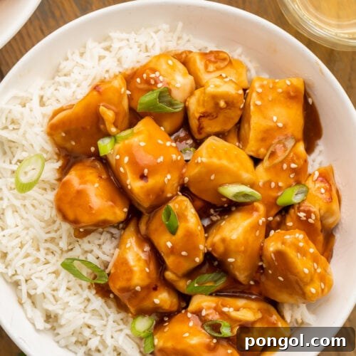 Orange glazed Instant Pot honey garlic chicken garnished with sesame seeds and sliced green onions in a bowl with white rice.
