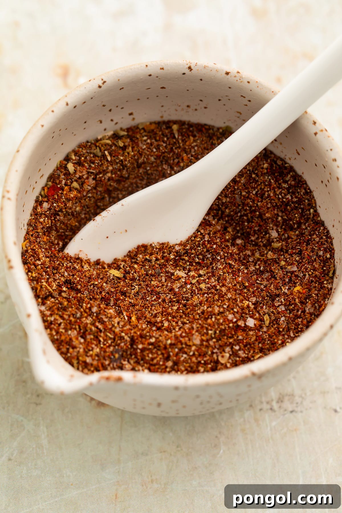 Overhead view of a small bowl filled with a rich, deep reddish-brown blend of spices for chicken taco seasoning.