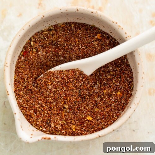 Overhead view of a small bowl filled with a rich, deep reddish-brown blend of spices for chicken taco seasoning.