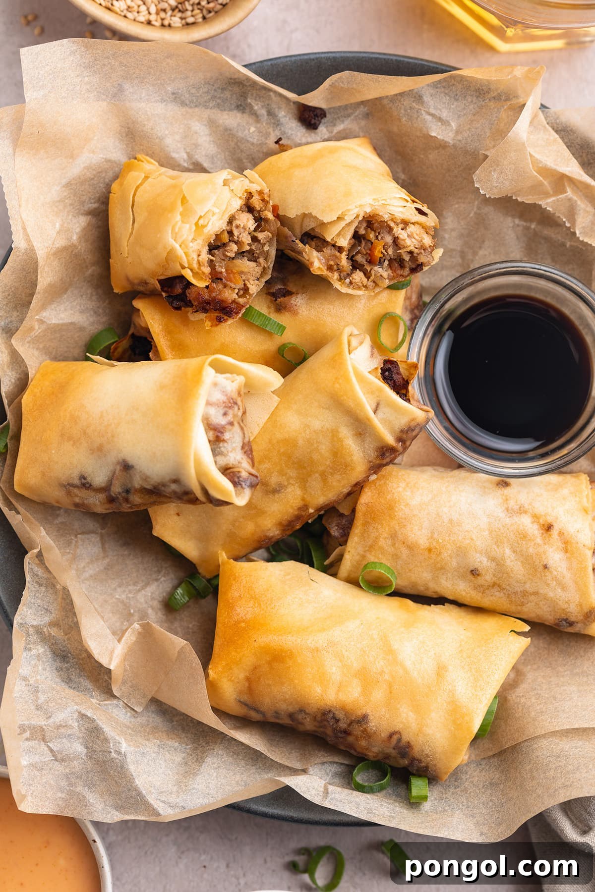 Top-down, overhead view of homemade air fryer egg rolls on a plate lined with parchment paper next to a small bowl of soy sauce.