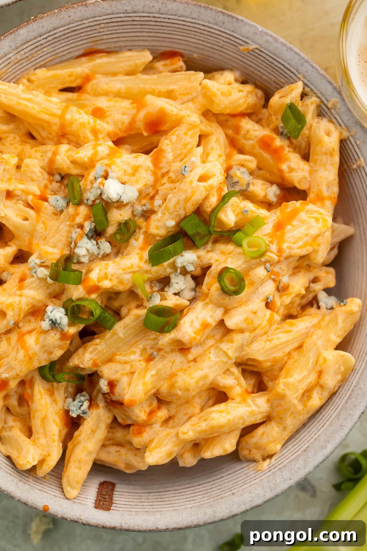 Close-up of an off-white bowl holding creamy buffalo chicken alfredo made with penne pasta and topped with sliced green onions, ready to be served.