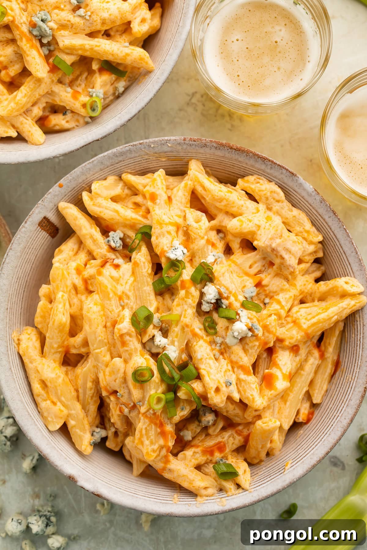 Overhead, zoomed out view of an off-white bowl of buffalo chicken alfredo made with penne pasta on a table, with a fork digging in.