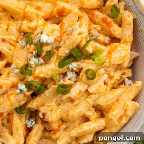 Close-up of an off-white bowl holding creamy buffalo chicken alfredo made with penne pasta and topped with sliced green onions.