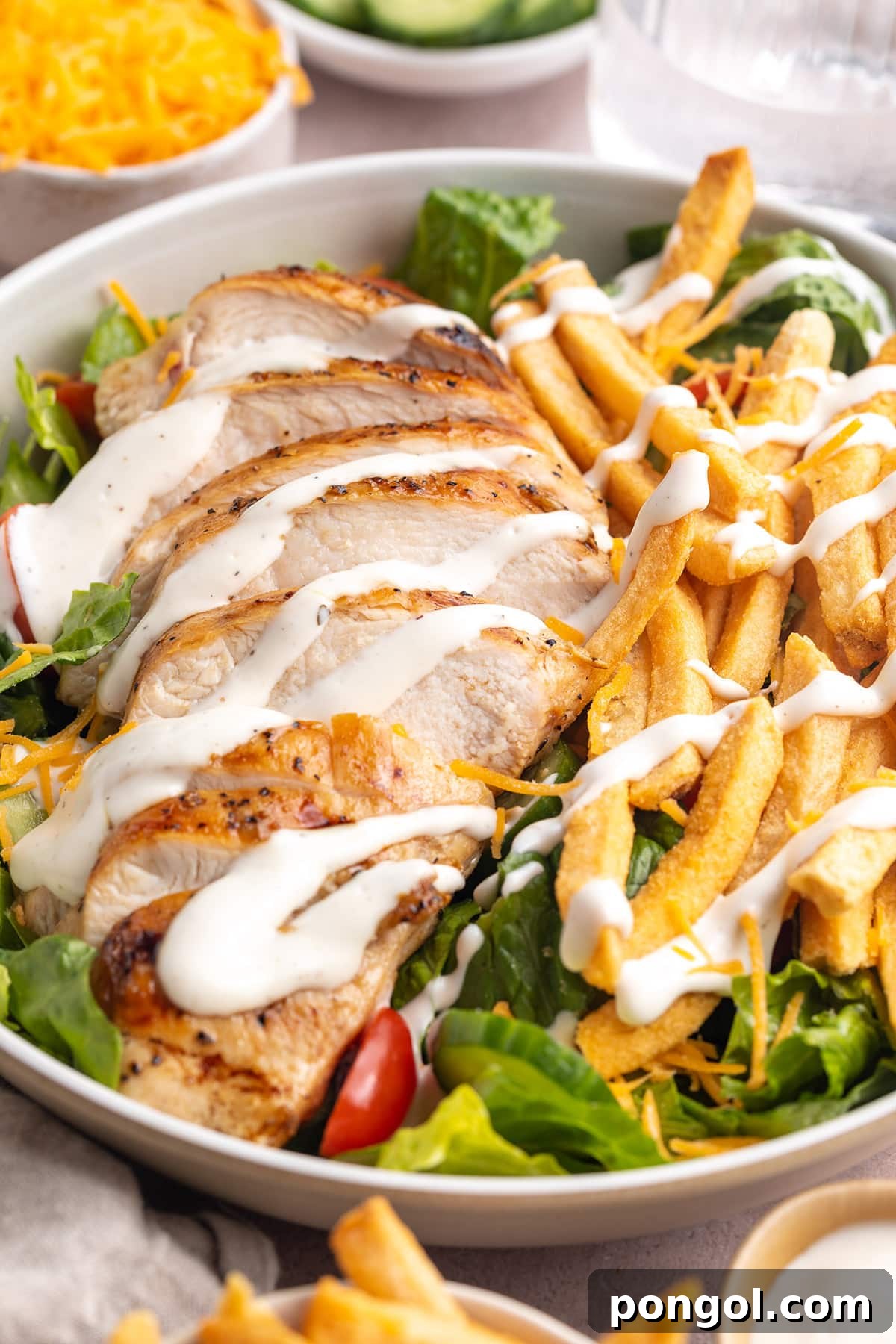 Angled view of a large bowl holding a Pittsburgh chicken salad with french fries and a drizzle of ranch dressing.