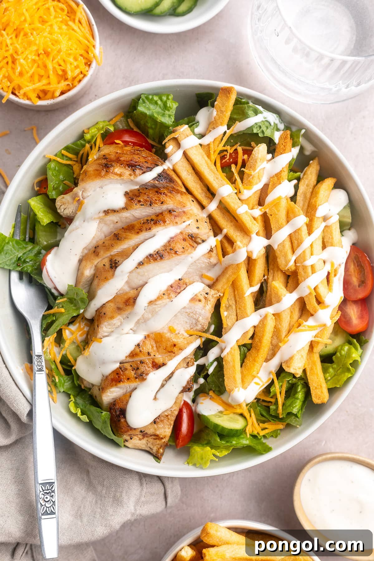 Zoomed out, top-down view of a Pittsburgh salad topped with sliced chicken, french fries, and ranch dressing.
