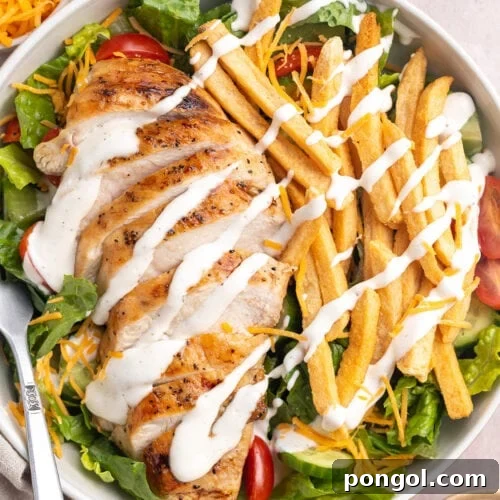 Zoomed out, top-down view of a Pittsburgh salad topped with sliced chicken, french fries, and ranch dressing.