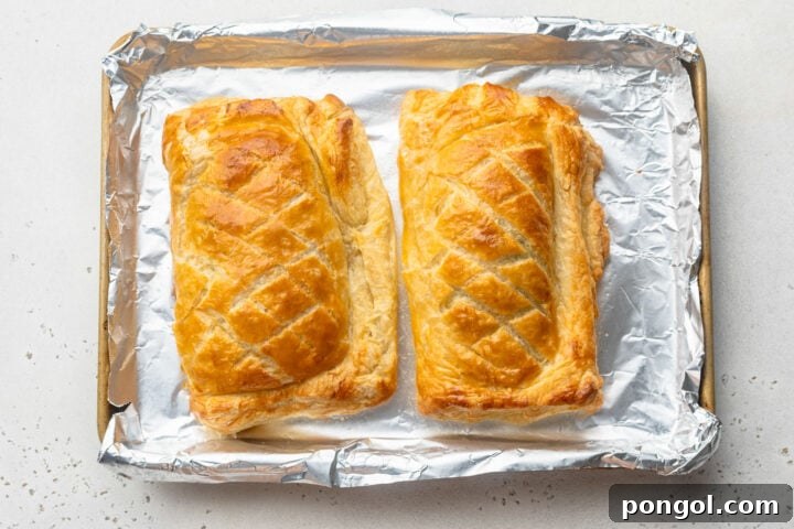 Fully baked, golden brown Salmon Wellingtons, scored with crosshatch patterns, on a baking sheet lined with parchment paper.