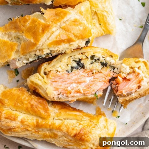 Salmon wellington, sliced and plated on a white round plate, with one slice placed on its side to show the salmon filling.