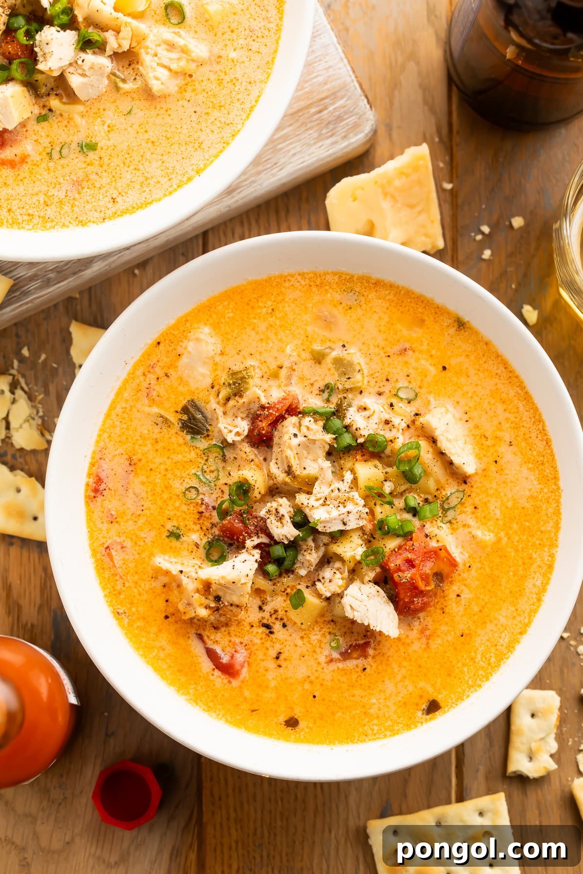 Overhead view of a bowl of Instant Pot cajun chicken pasta soup on a dark wooden table surrounded by broken saltine crackers.
