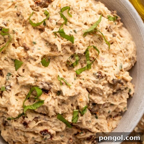 A close-up look at a large neutral bowl holding marry me chicken salad, with sun dried tomatoes and fresh basil.