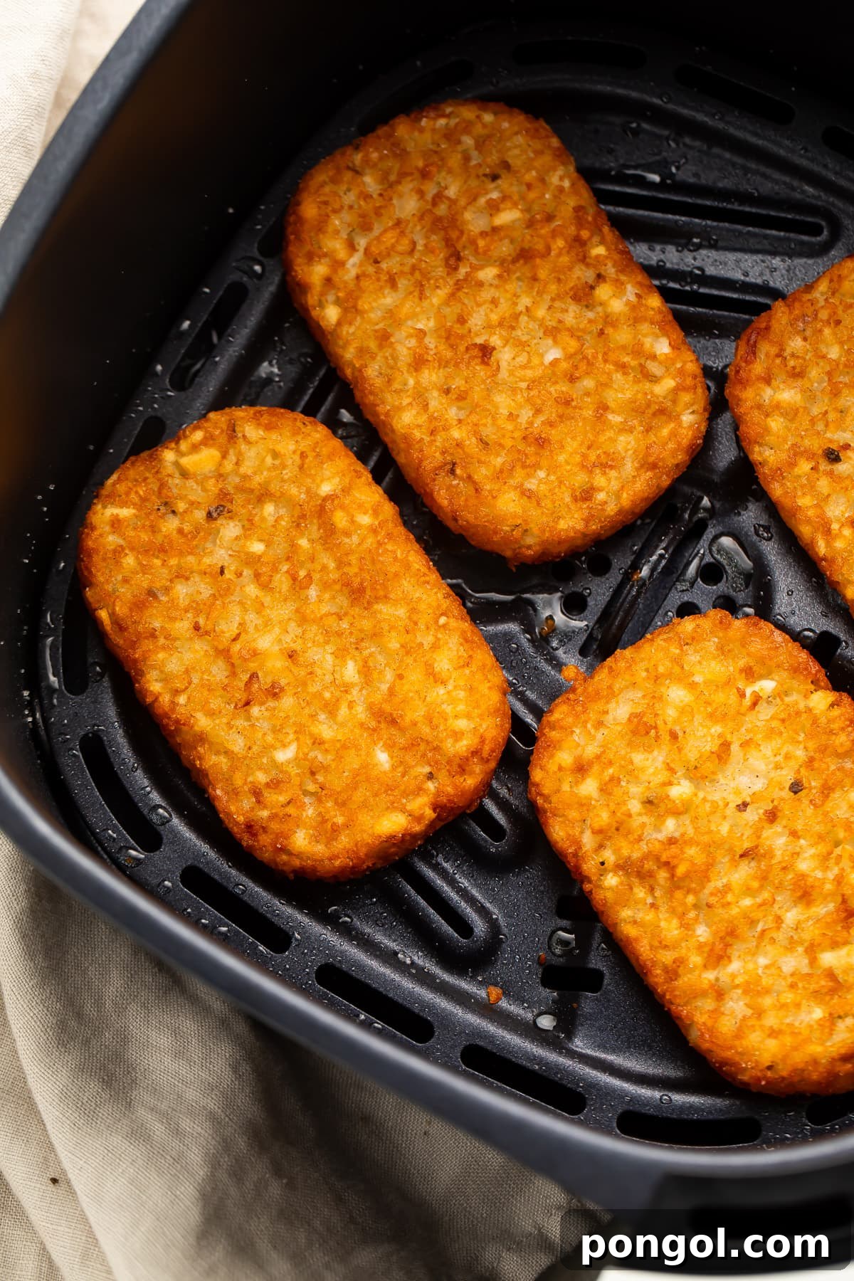 Four golden and crispy hash brown patties resting in an air fryer basket after cooking.