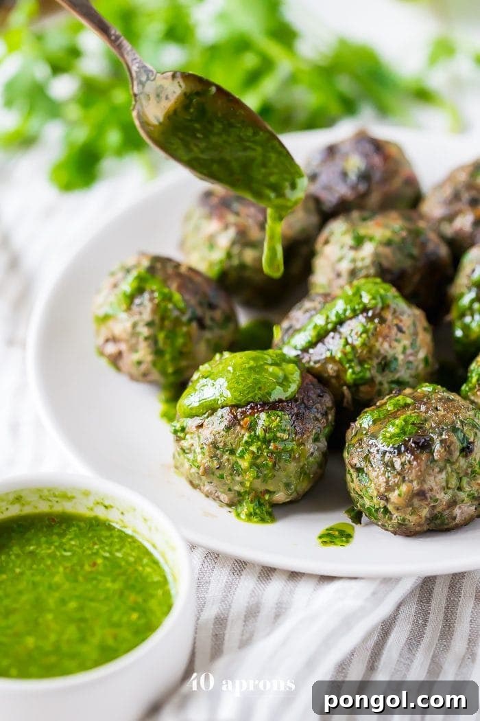 Close-up of golden-brown chimichurri Whole30 meatballs on a plate, garnished with fresh chimichurri sauce.