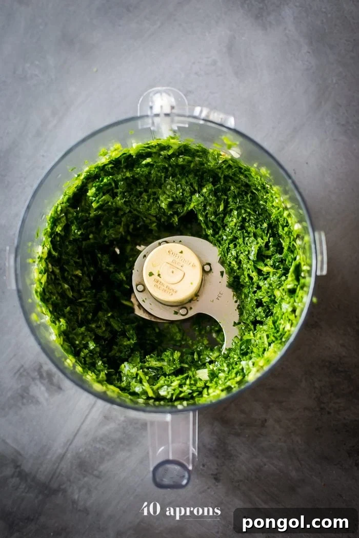 Hand holding a fork with a chimichurri Whole30 meatball, showcasing its tender texture and vibrant sauce.