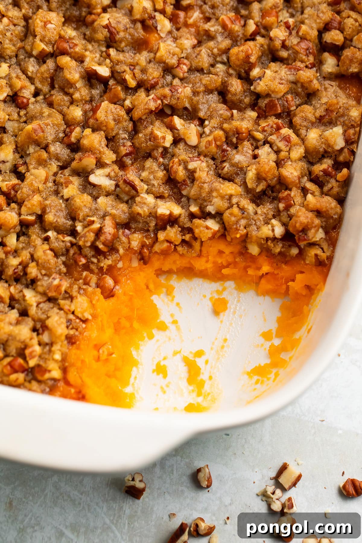Ruth's Chris Signature Sweet Potato Casserole 3 A serving of Ruth's Chris Sweet Potato Casserole scooped out from a larger dish, showing the creamy sweet potato base and the crunchy pecan praline topping. Perfect for a holiday feast.