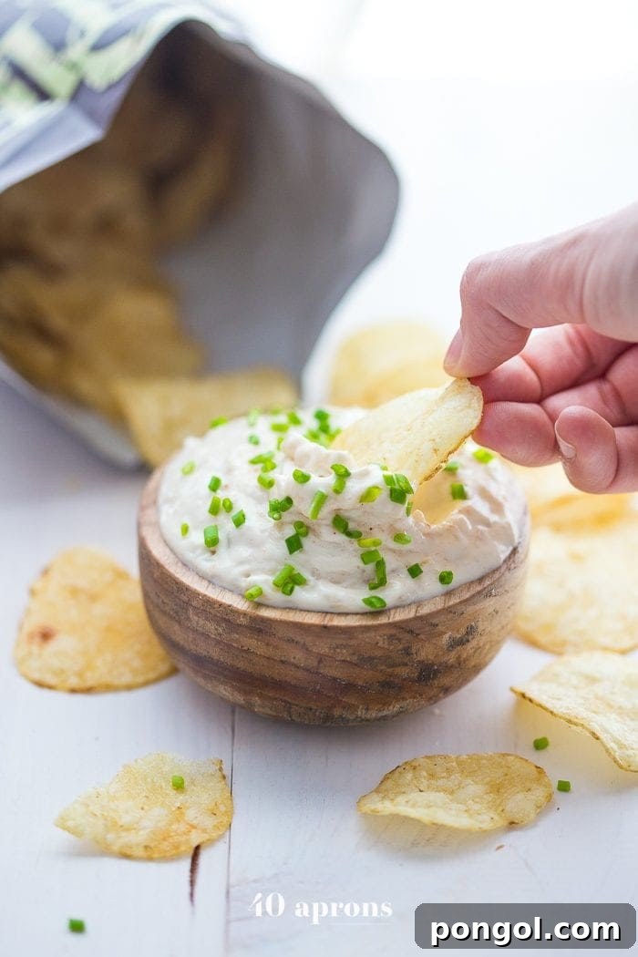 Creamy Paleo French Onion Dip served in a bowl with Kettle Brand Avocado Oil Chips around it on a wooden board.